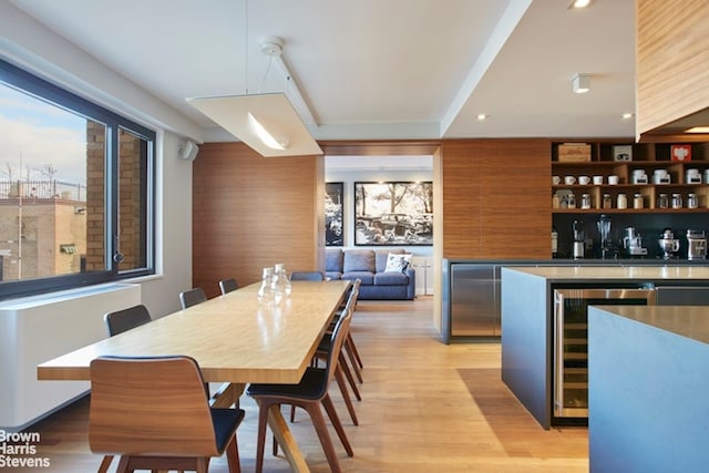 dining room featuring wine cooler, plenty of natural light, light wood finished floors, and a community bar