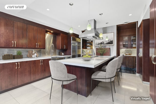 kitchen featuring sink, hanging light fixtures, a kitchen breakfast bar, island exhaust hood, and built in fridge