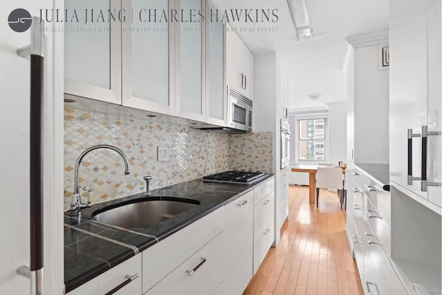 kitchen featuring sink, white cabinetry, appliances with stainless steel finishes, light hardwood / wood-style floors, and backsplash