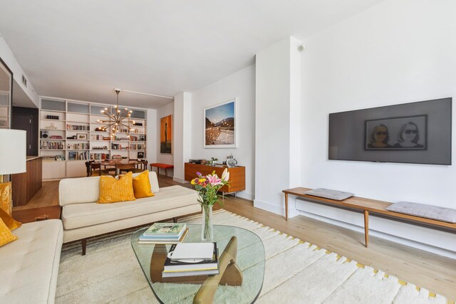 living room with a notable chandelier, light wood-type flooring, and built in shelves