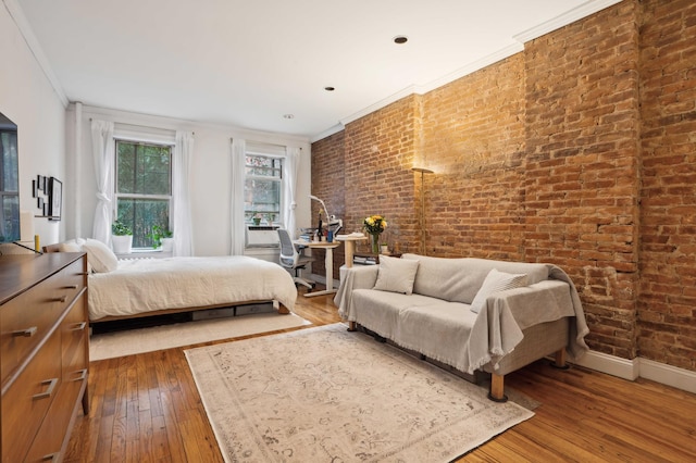 bedroom featuring hardwood / wood-style flooring, ornamental molding, brick wall, and baseboards