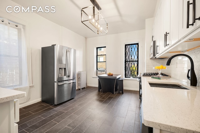 kitchen with a sink, backsplash, radiator, appliances with stainless steel finishes, and dark wood-style flooring