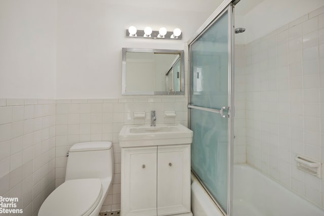 full bathroom with vanity, combined bath / shower with glass door, tile walls, and toilet