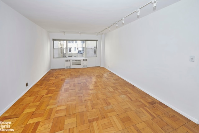 empty room featuring light parquet flooring, rail lighting, and radiator