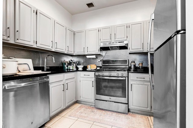 kitchen featuring light tile patterned floors, under cabinet range hood, stainless steel appliances, visible vents, and dark countertops