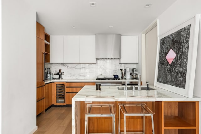 kitchen with open shelves, beverage cooler, wall chimney range hood, tasteful backsplash, and a sink