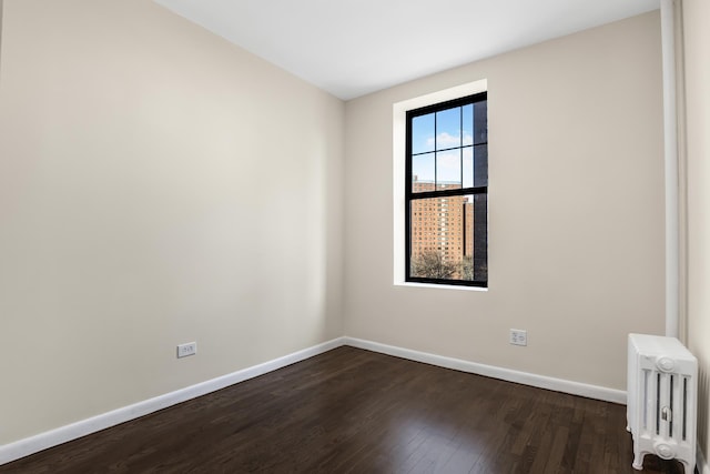 unfurnished room featuring dark wood-style flooring, baseboards, and radiator heating unit