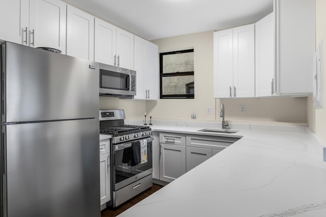 kitchen with stainless steel appliances, white cabinets, a sink, and light stone counters