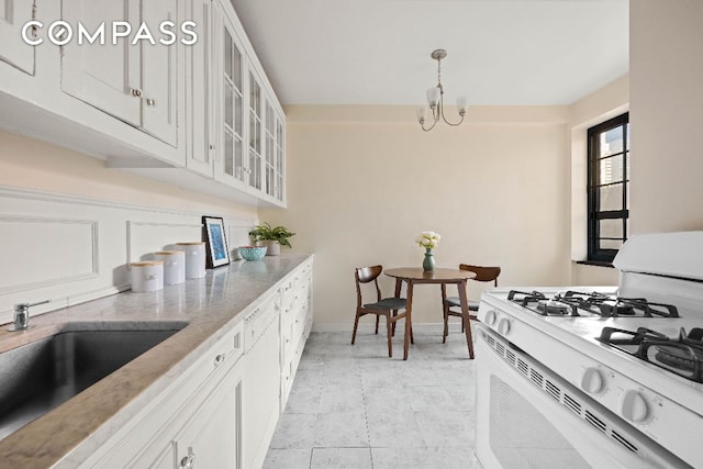 kitchen featuring sink, white cabinets, light tile patterned floors, a notable chandelier, and gas range gas stove