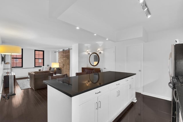 kitchen with dark wood-type flooring, a barn door, stainless steel fridge, white cabinets, and track lighting