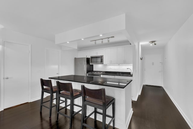 kitchen featuring appliances with stainless steel finishes, backsplash, white cabinetry, a kitchen breakfast bar, and dark wood-type flooring