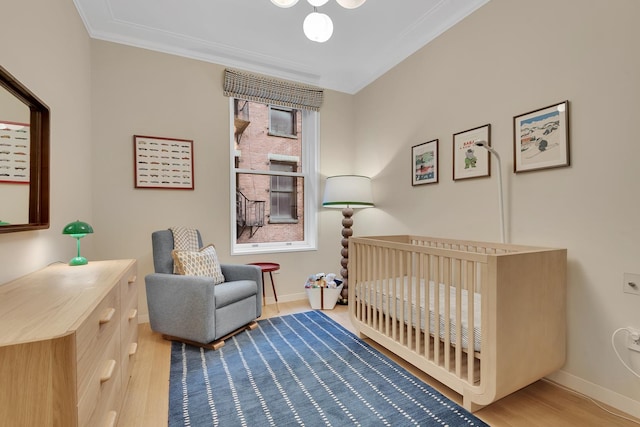 bedroom featuring wood finished floors, a crib, baseboards, and ornamental molding