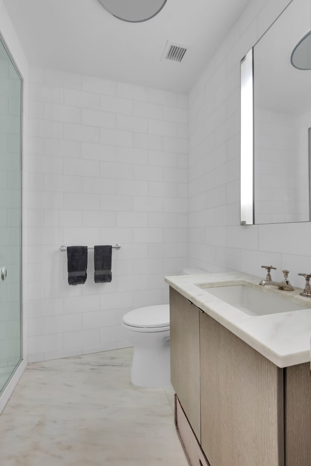 bathroom with tile walls, visible vents, toilet, and vanity