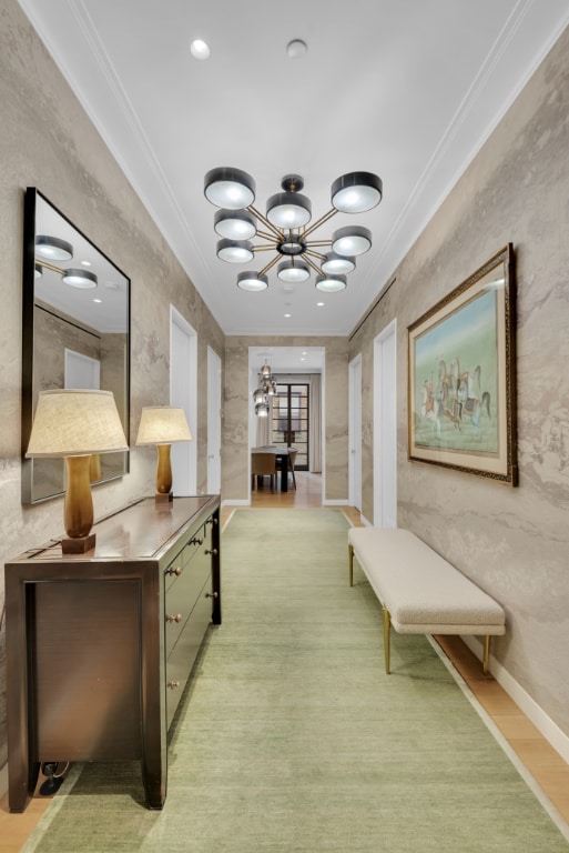 corridor with an inviting chandelier, ornamental molding, and light wood-type flooring