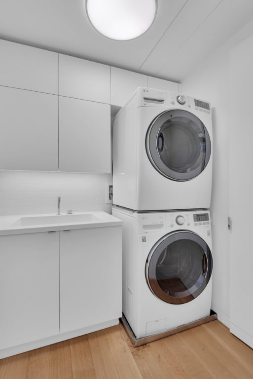 laundry room featuring stacked washer and dryer, cabinets, light hardwood / wood-style floors, and sink