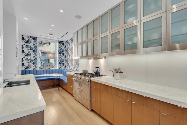 kitchen featuring stainless steel gas stovetop, sink, light stone counters, and light wood-type flooring