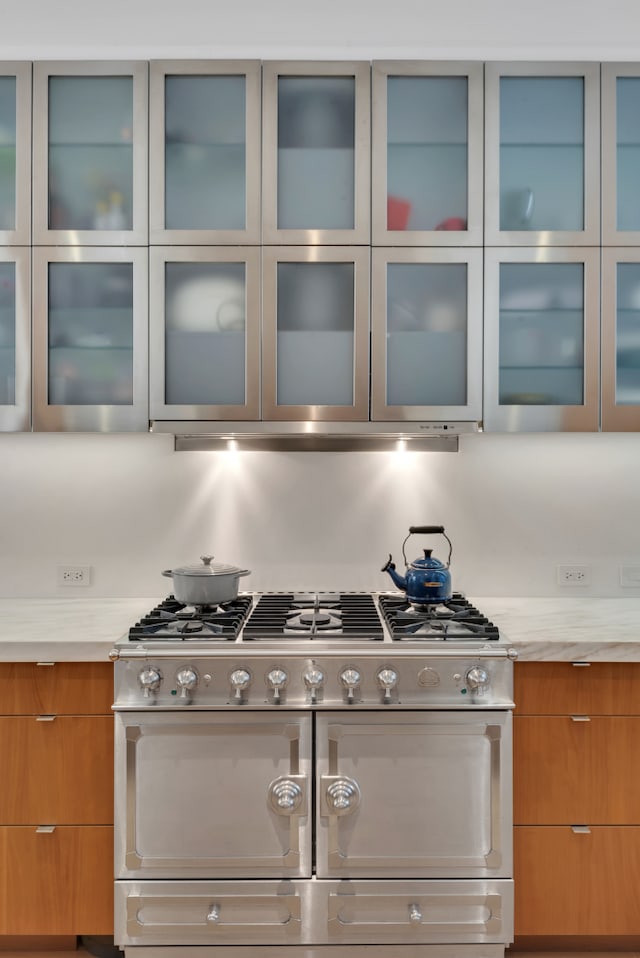kitchen with double oven range, modern cabinets, decorative backsplash, glass insert cabinets, and brown cabinets