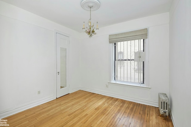 spare room featuring radiator, hardwood / wood-style flooring, and a notable chandelier