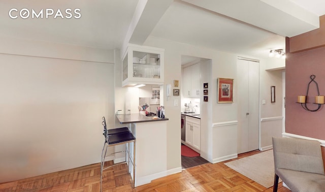 kitchen featuring a peninsula, a breakfast bar, white cabinetry, dark countertops, and glass insert cabinets