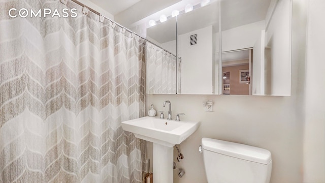 full bath featuring visible vents, toilet, a shower with shower curtain, and a sink