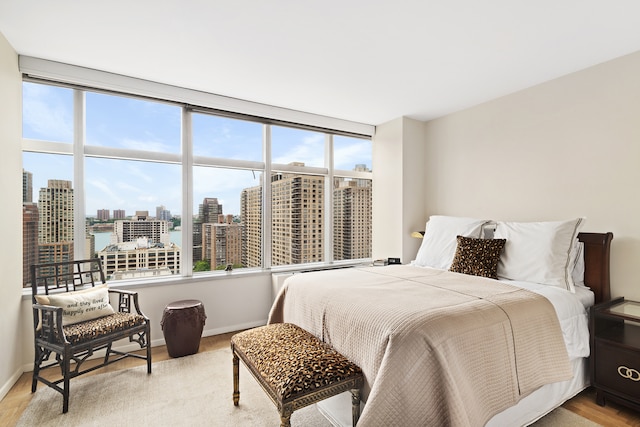 bedroom with baseboards, multiple windows, a city view, and light wood-type flooring