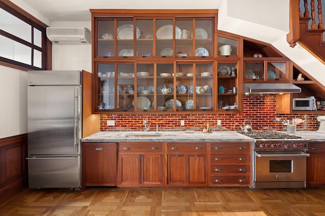 kitchen featuring an AC wall unit, a sink, premium appliances, range hood, and light stone countertops