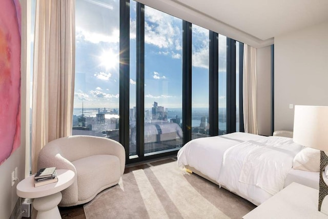 bedroom with a view of city, floor to ceiling windows, wood finished floors, and access to exterior