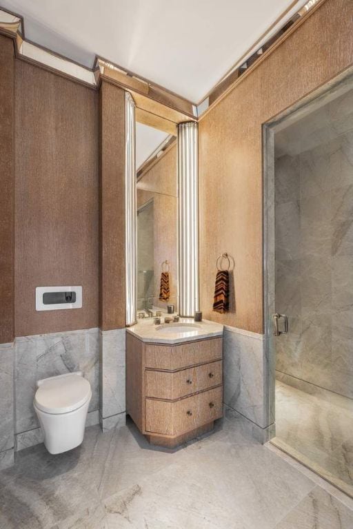 bathroom with walk in shower, vanity, toilet, and tile walls