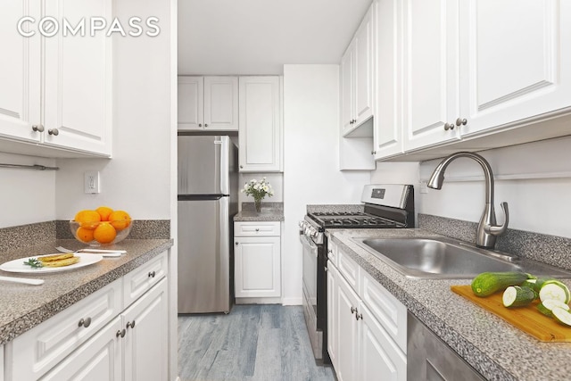 kitchen with stainless steel appliances, white cabinetry, sink, and light hardwood / wood-style flooring