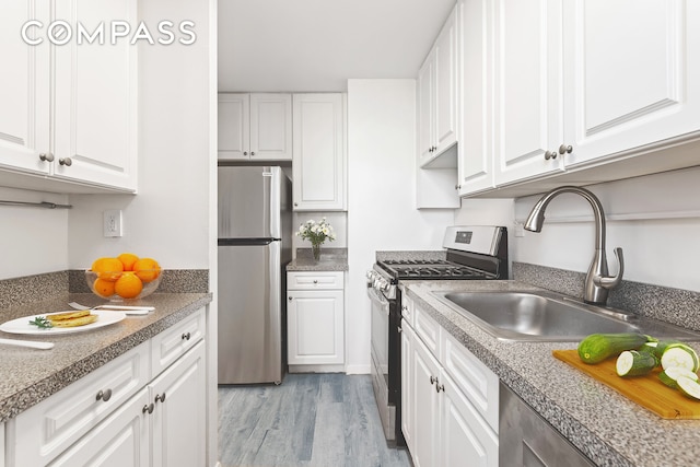 kitchen featuring light wood-style floors, appliances with stainless steel finishes, white cabinetry, and a sink