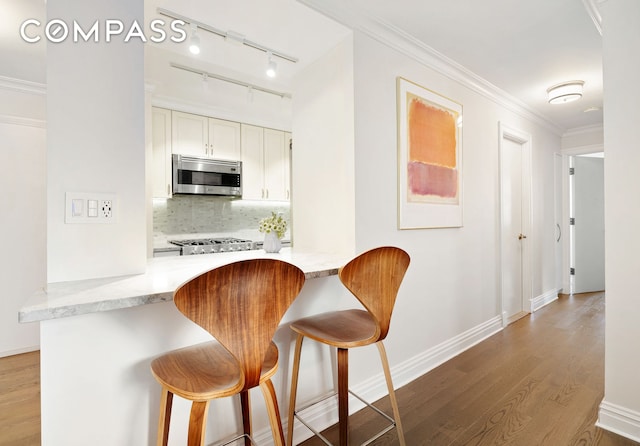 kitchen featuring stainless steel microwave, a kitchen breakfast bar, wood finished floors, and crown molding