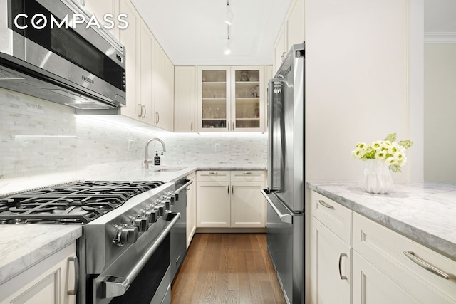 kitchen with appliances with stainless steel finishes, a sink, dark wood-style flooring, and light stone countertops