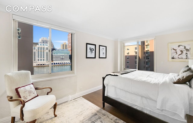 bedroom featuring wood finished floors, a city view, ornamental molding, and baseboards
