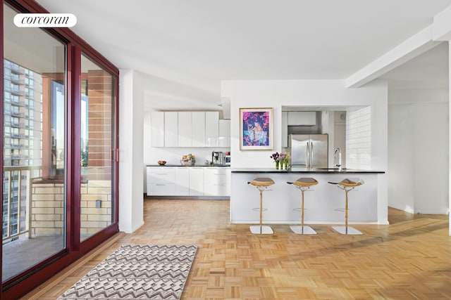 kitchen featuring white cabinets, dark countertops, modern cabinets, freestanding refrigerator, and a kitchen bar