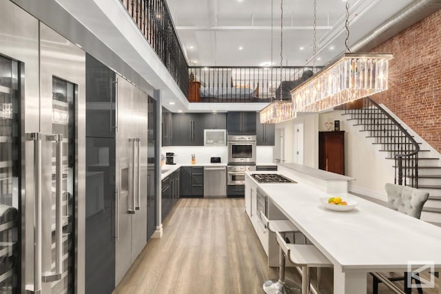 kitchen with a breakfast bar, pendant lighting, a towering ceiling, light hardwood / wood-style floors, and stainless steel appliances