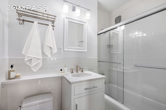 full bathroom with vanity, combined bath / shower with glass door, tile walls, and toilet