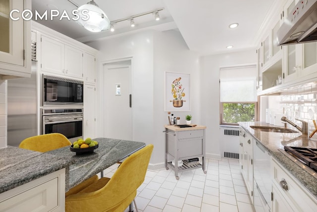 kitchen with sink, appliances with stainless steel finishes, radiator, light stone countertops, and white cabinets