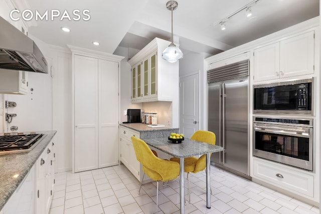 kitchen featuring white cabinetry, light stone countertops, built in appliances, and range hood