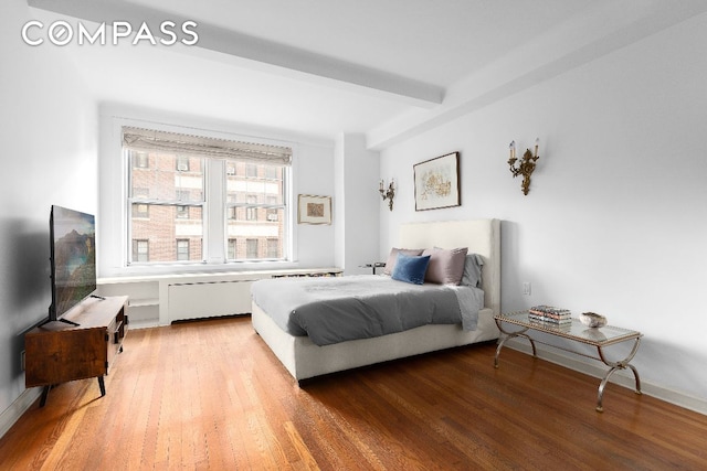 bedroom featuring beamed ceiling, radiator, and hardwood / wood-style floors