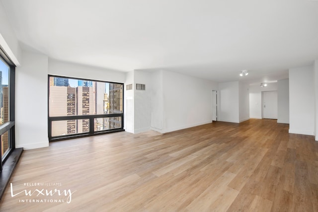 unfurnished living room featuring light wood-type flooring, visible vents, and baseboards