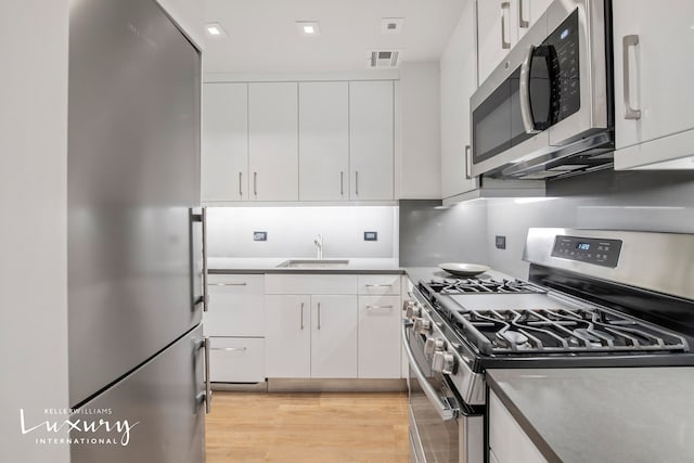 kitchen featuring stainless steel appliances, light wood-type flooring, white cabinets, and a sink