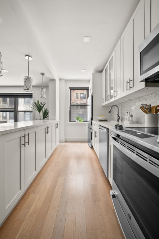 kitchen with decorative light fixtures, light hardwood / wood-style flooring, stainless steel appliances, and white cabinets