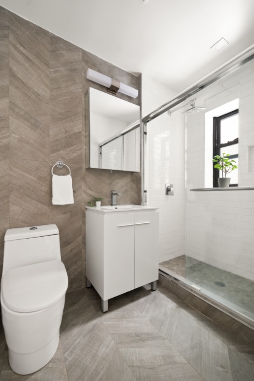 bathroom with tile walls, vanity, a shower with shower door, tile patterned floors, and toilet