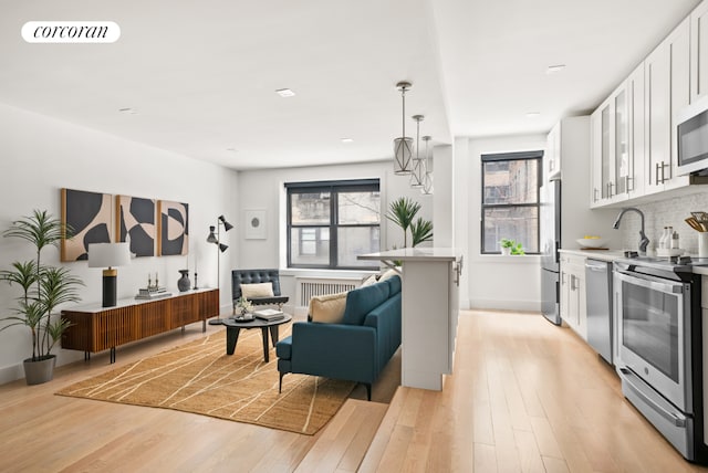 kitchen featuring white cabinetry, stainless steel appliances, radiator, and light wood-type flooring