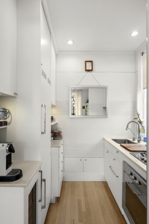 kitchen featuring light countertops, white cabinets, oven, and a sink