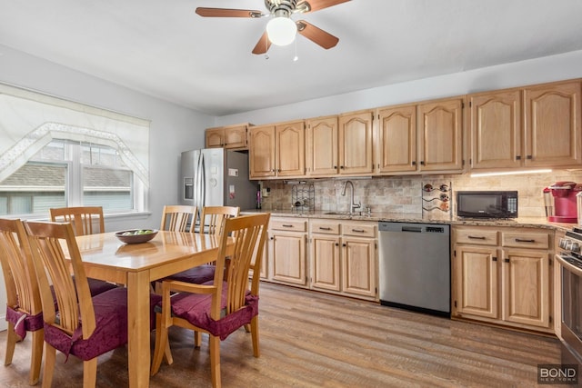 kitchen with light stone counters, light wood-style flooring, stainless steel appliances, a sink, and backsplash