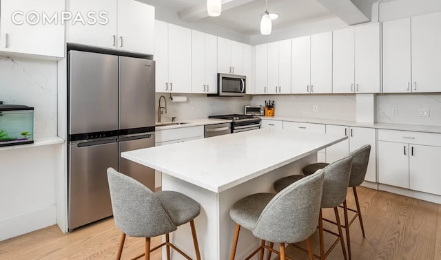 kitchen with appliances with stainless steel finishes, white cabinets, a sink, and a breakfast bar area