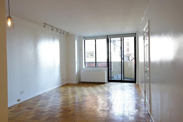 spare room featuring light parquet floors, rail lighting, radiator, and a wall of windows