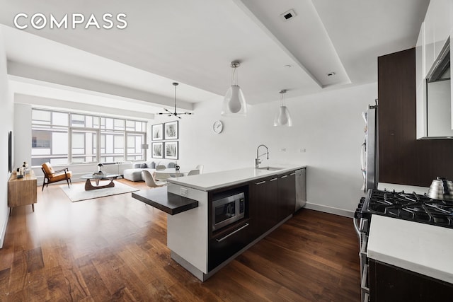 kitchen featuring stainless steel appliances, light countertops, dark wood-type flooring, a sink, and a peninsula