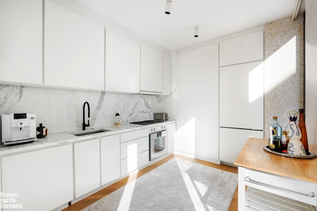 kitchen featuring sink, light stone counters, wall oven, decorative backsplash, and white cabinets